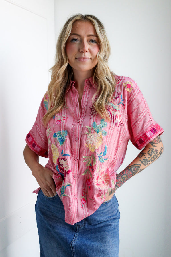 Woman wearing a pink floral embroidered shirt against a white background
