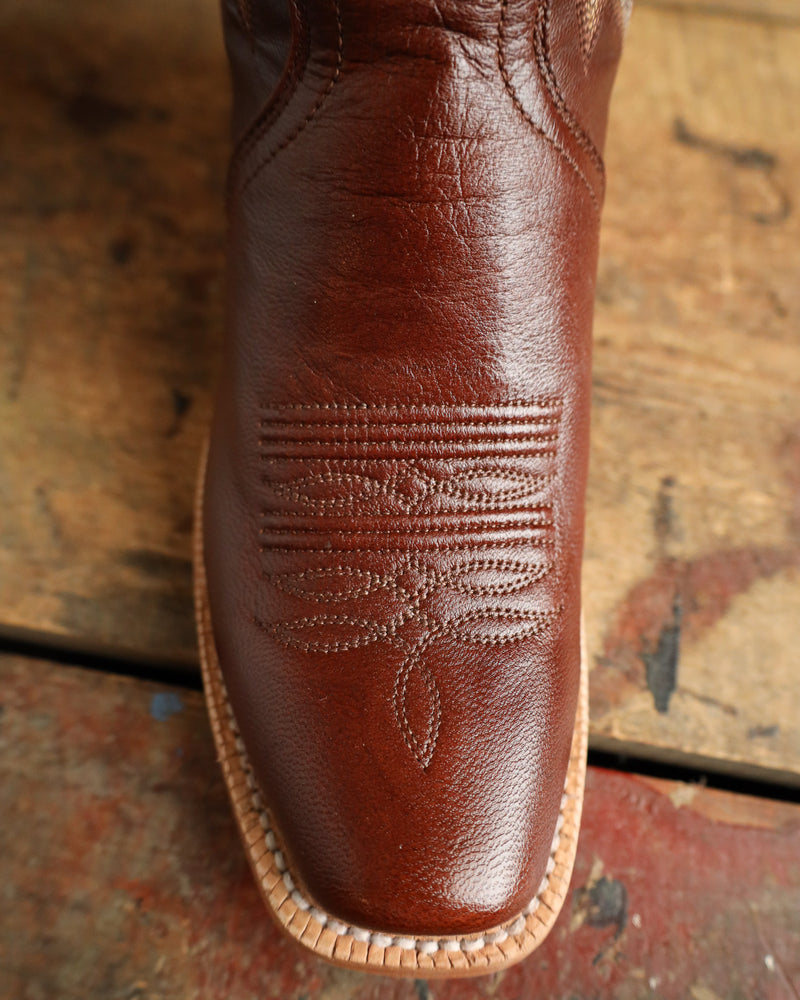 Close-up of a brown leather boot with intricate stitching on a rustic wooden surface.
