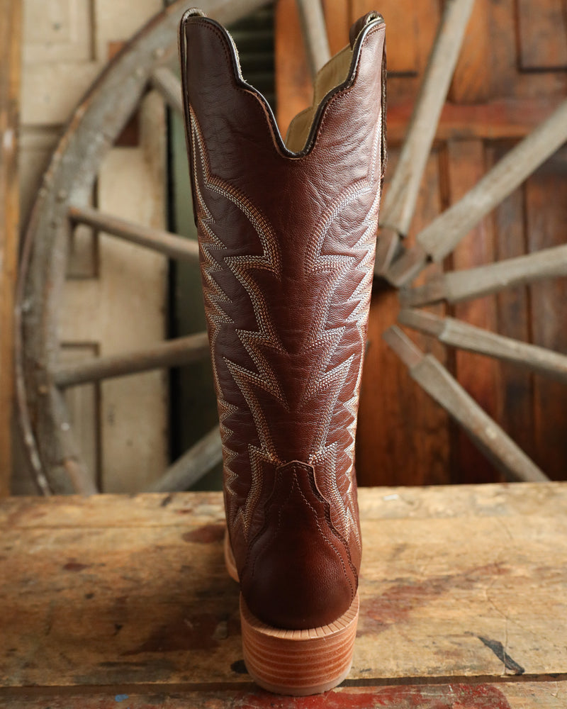 Brown cowboy boot with intricate stitching on a wooden surface with a rustic background