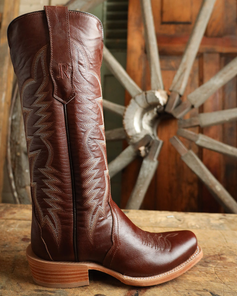 Brown leather boot with intricate stitching on a wooden surface with a rustic background