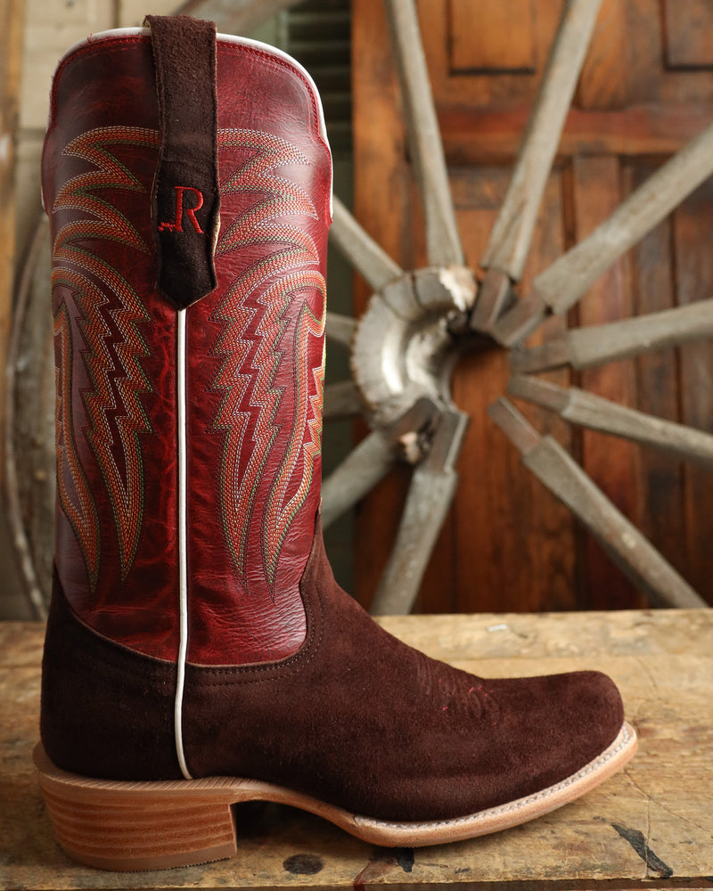 Brown and red cowboy boot with intricate design on a wooden surface with a rustic wheel background