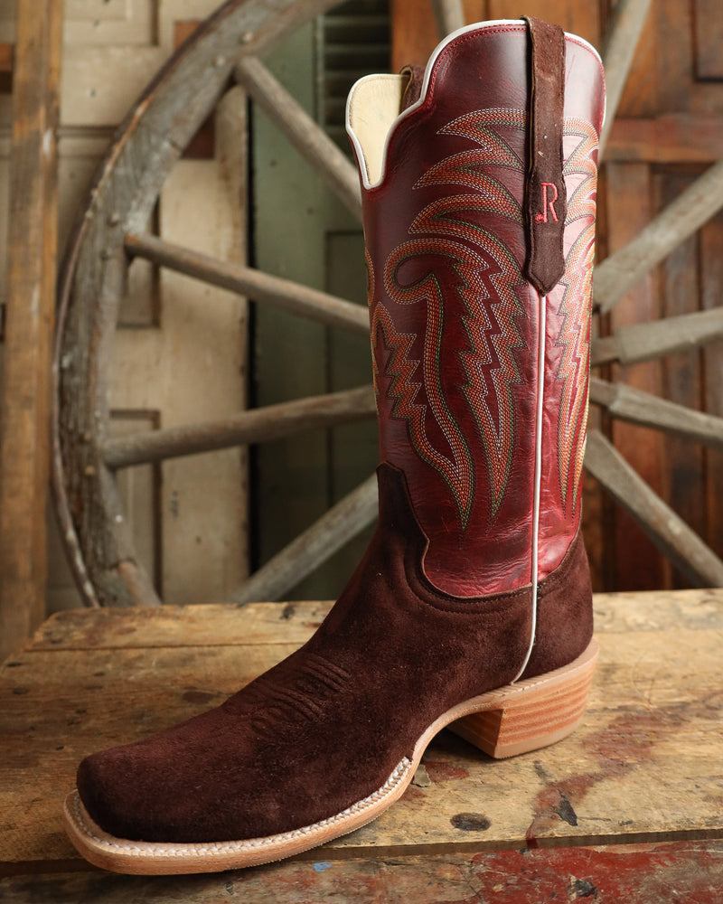 Brown cowboy boot with intricate design on a wooden surface with a rustic background