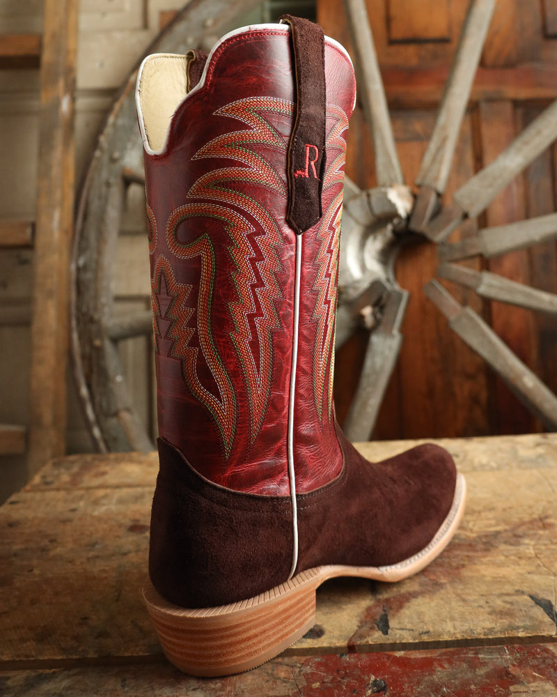 Red and brown cowboy boot with intricate design on a wooden surface with a wheel in the background