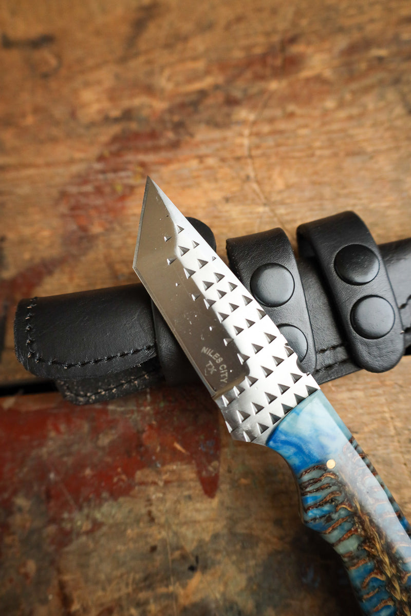 Knife with a textured blade and blue handle in a black sheath on a wooden surface