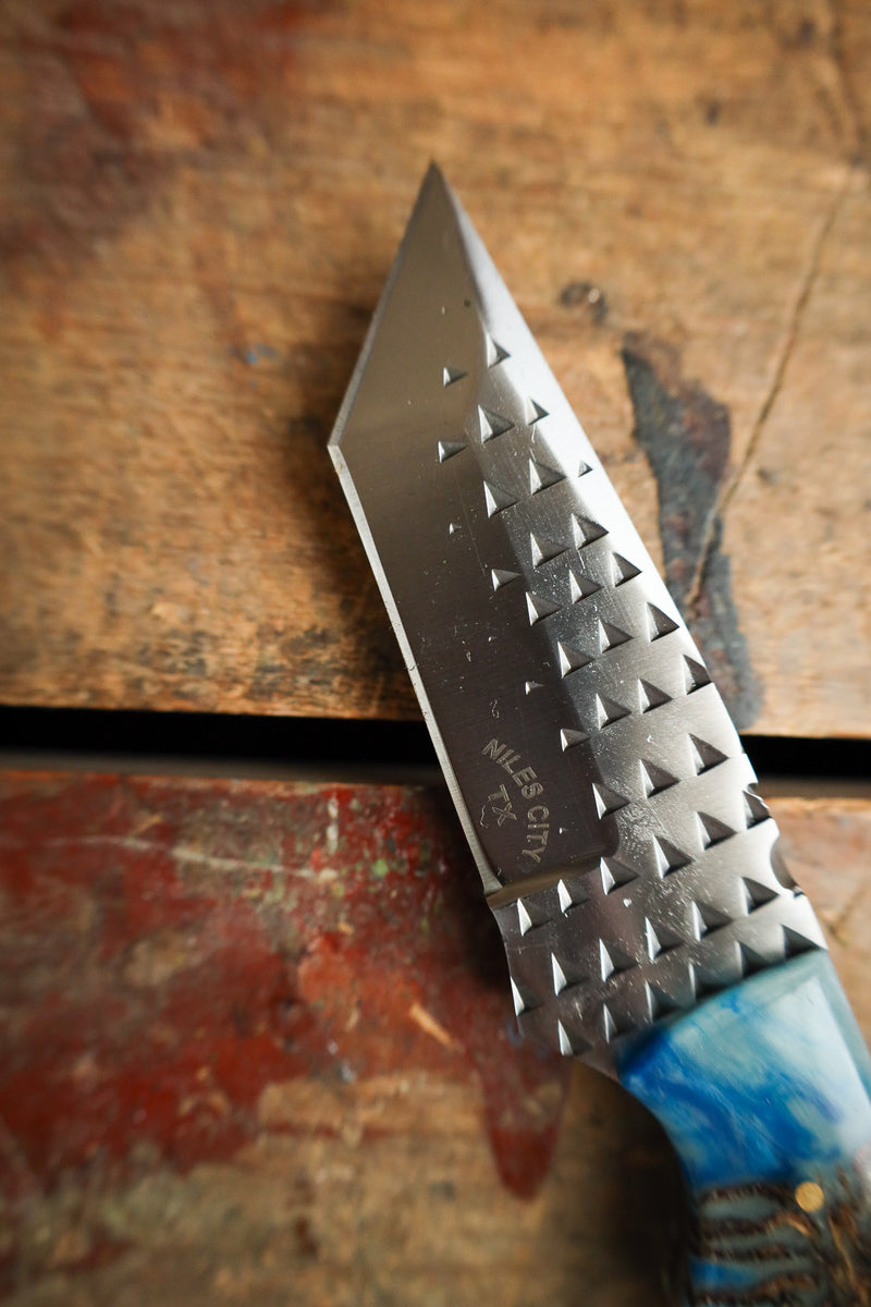 Knife with a textured blade and blue handle on a wooden surface