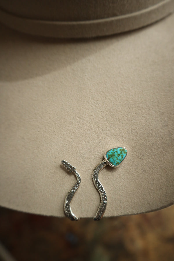 Silver earrings with a turquoise stone on a beige surface