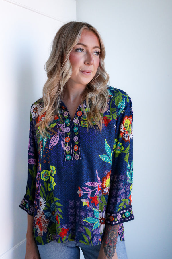 Woman wearing a colorful floral blouse against a white wall