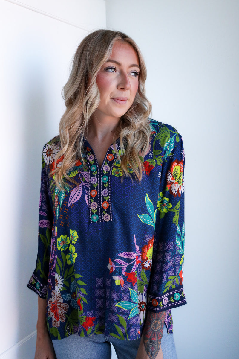 Woman wearing a colorful floral blouse against a white wall