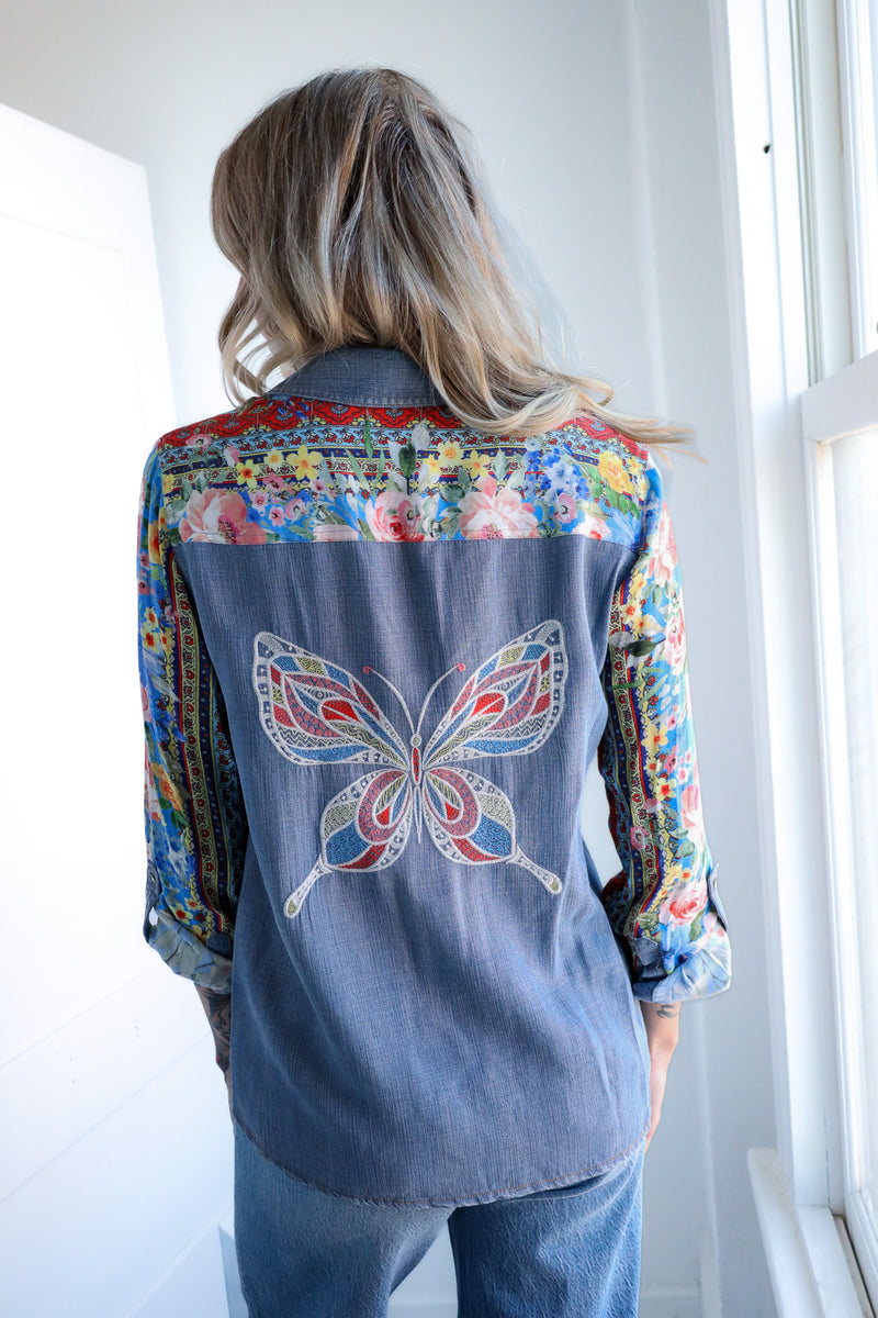 Person wearing a denim shirt with colorful butterfly design and floral patterns.