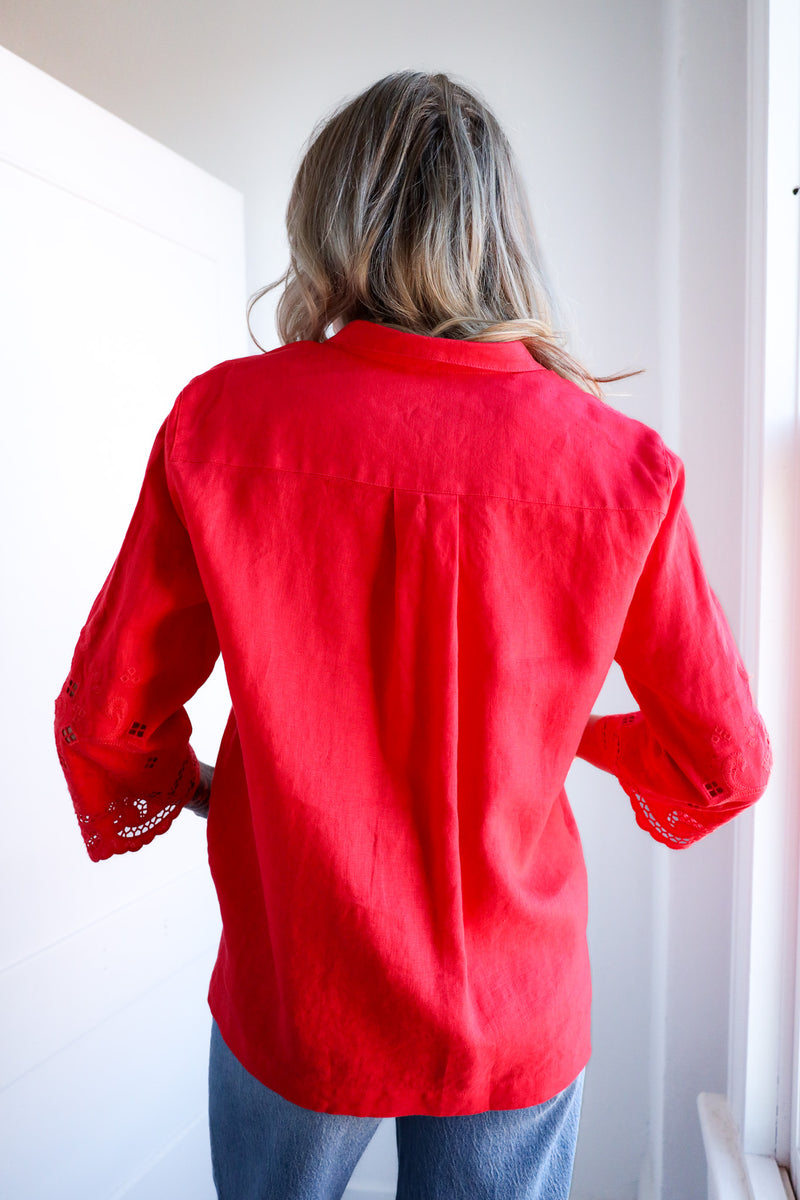 Person wearing a red blouse with lace cuffs in a bright room.