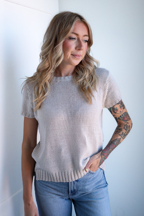 Woman wearing a light beige sweater and blue jeans against a white wall