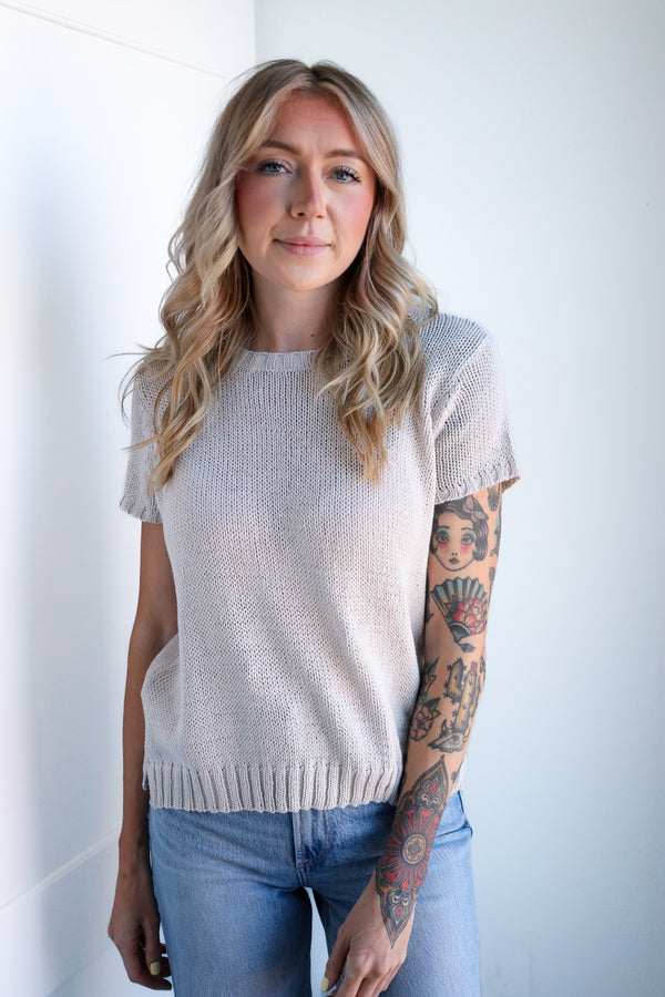 Woman wearing a light-colored knit top and blue jeans against a white background