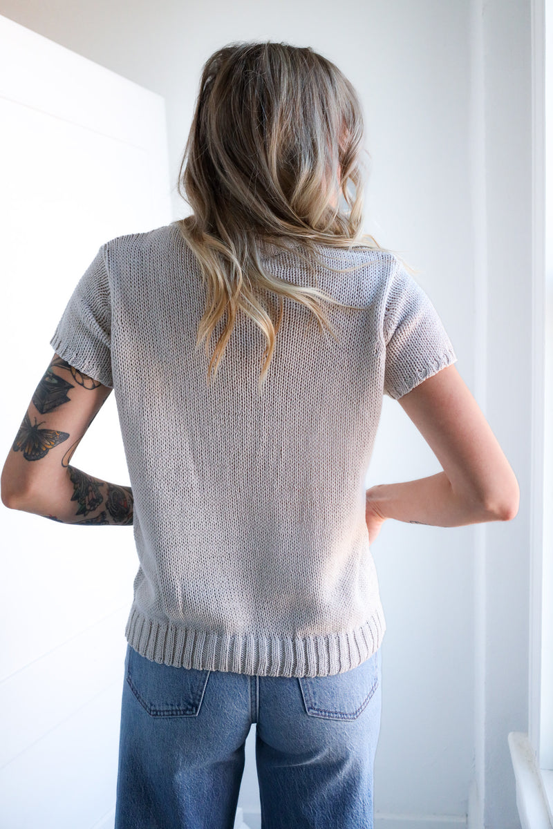 Person wearing a light beige knit cardigan and blue jeans against a white background