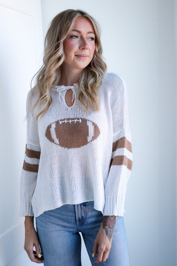 Woman wearing a white sweater with a football design and blue jeans against a light background