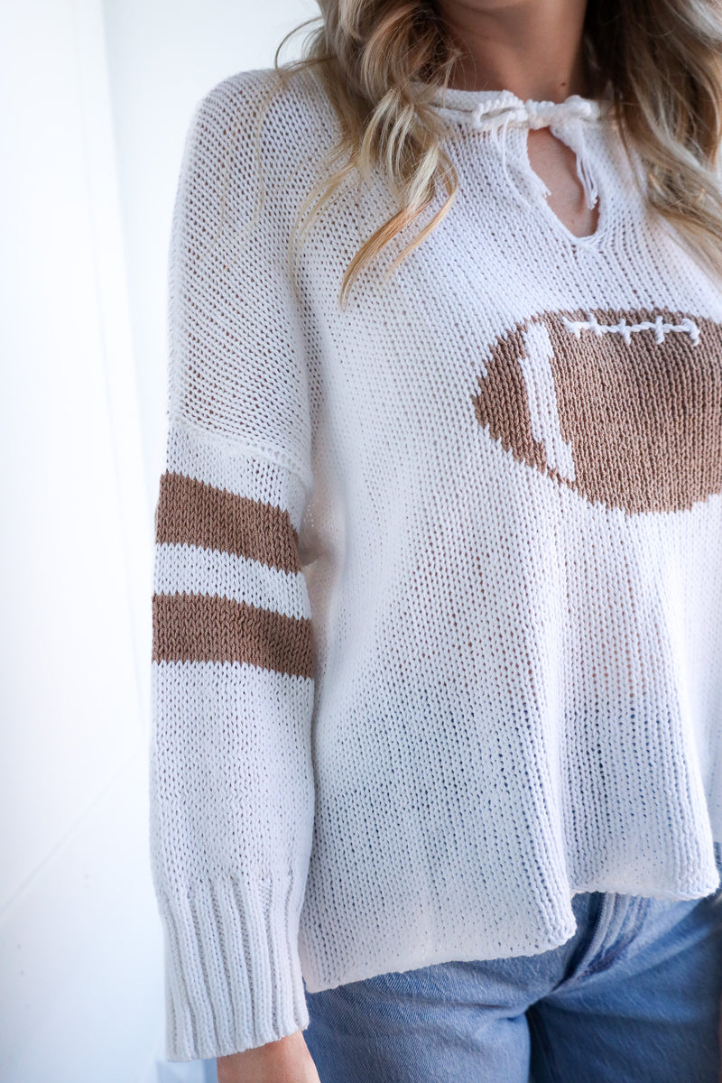White sweater with brown football design and stripes on a white background