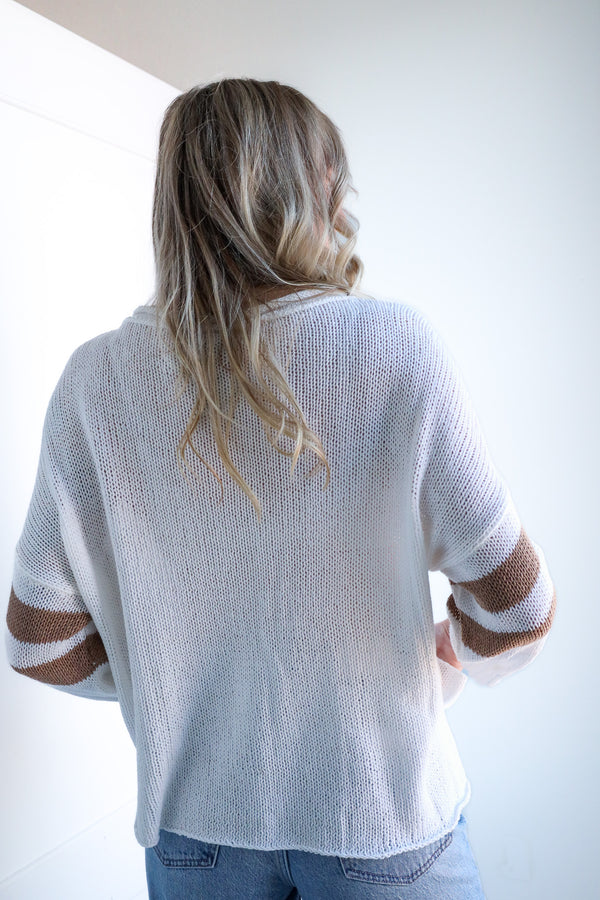 Person wearing a white sweater with sheer sleeves against a white background