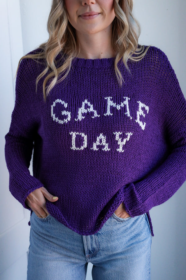 Person wearing a purple sweater with 'GAME DAY' text against a white background