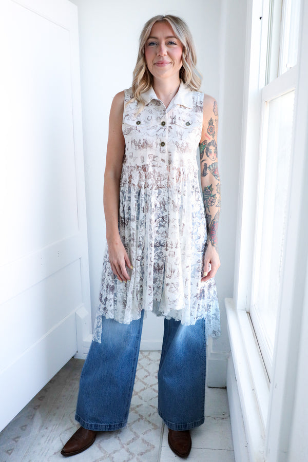 Woman wearing a sleeveless floral dress over a denim jumpsuit in a bright room.