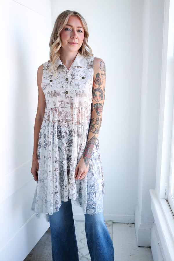 Woman wearing a sleeveless patterned top and jeans in a minimal white room.
