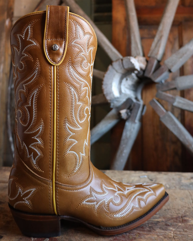 Brown cowboy boot with intricate white embroidery on a wooden surface with a rustic background.