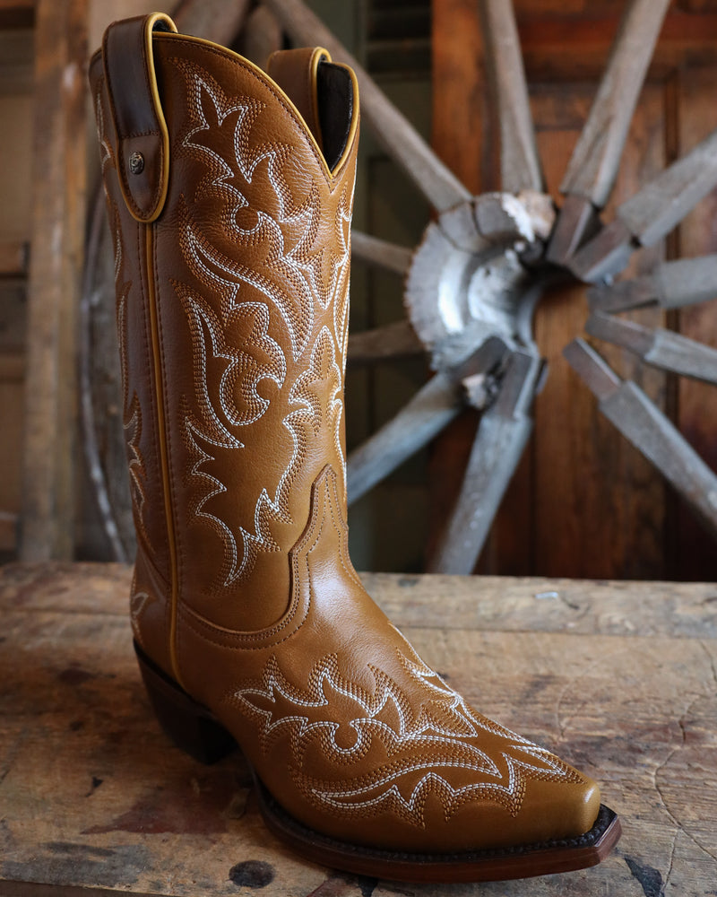 Brown cowboy boot with white embroidery on a wooden surface with a rustic background