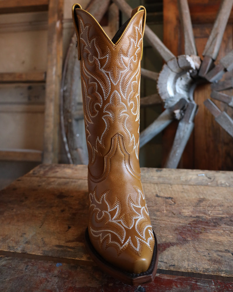 Brown cowboy boot with white embroidery on a wooden surface with a wagon wheel in the background