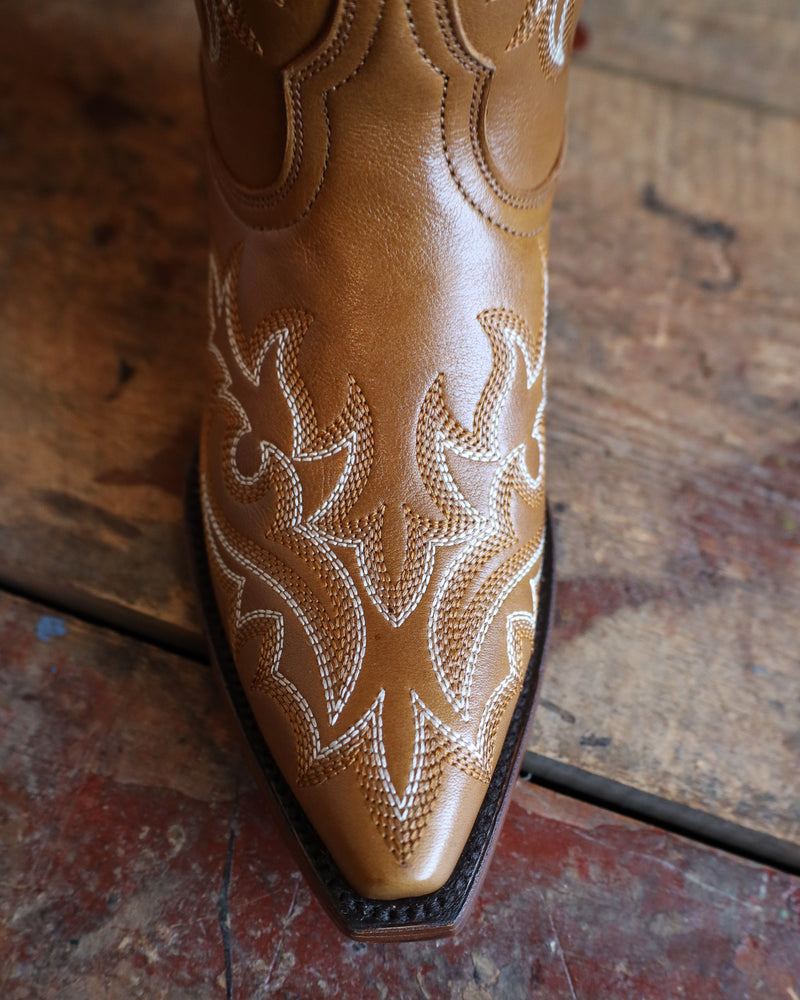 Tan cowboy boot with white embroidery on a wooden floor