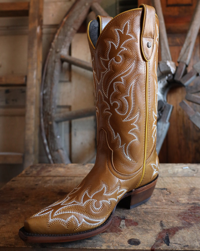 Brown cowboy boot with intricate white embroidery on a wooden surface with rustic background