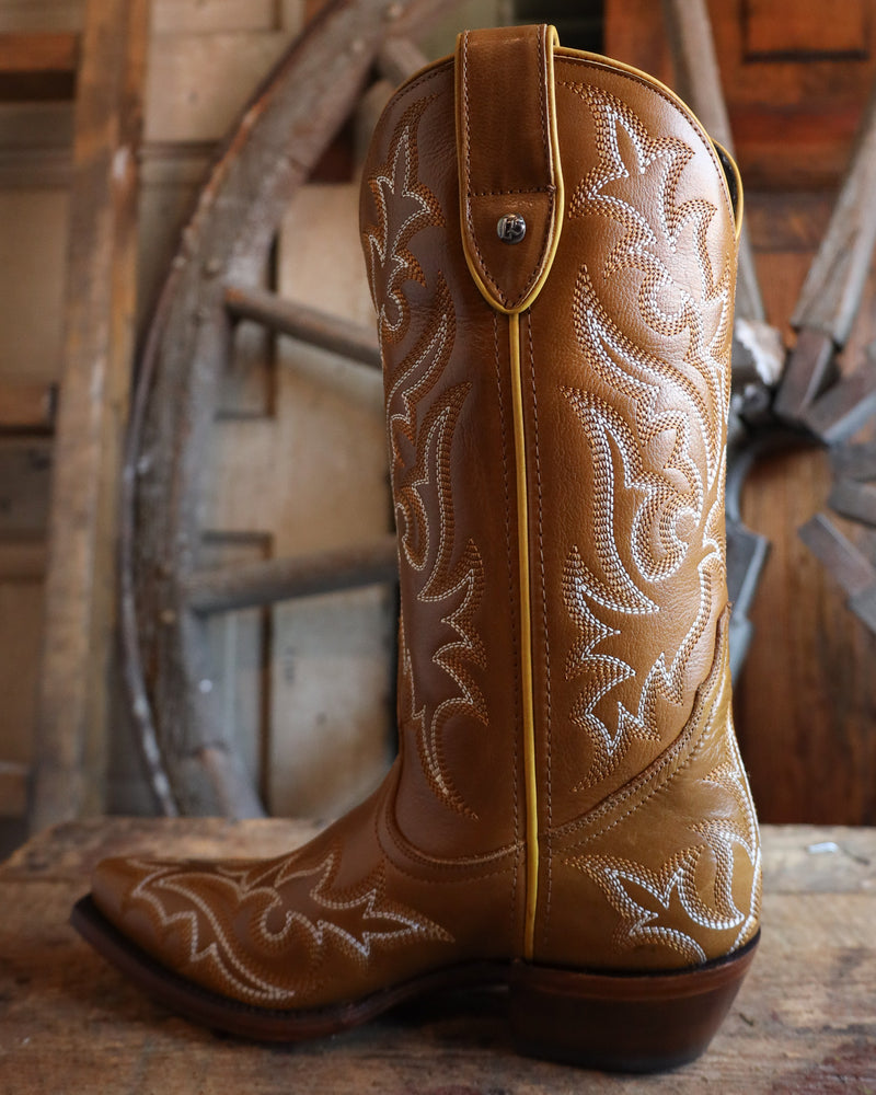 Brown cowboy boot with intricate white embroidery on a rustic wooden background