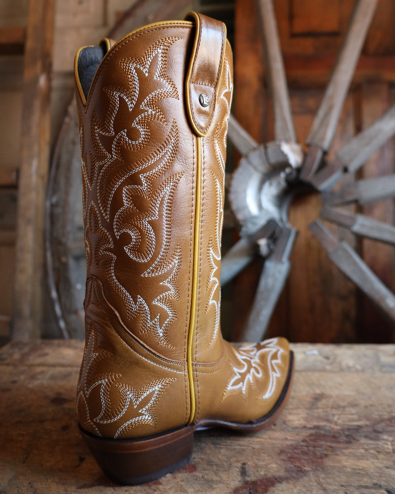 Brown cowboy boot with intricate white embroidery on a wooden surface with a rustic background.