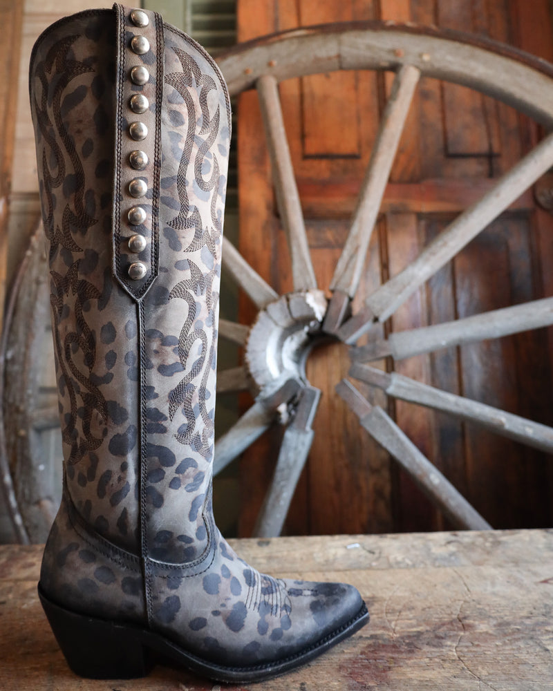 Leopard print boot with studded details on a wooden surface with a rustic wheel background