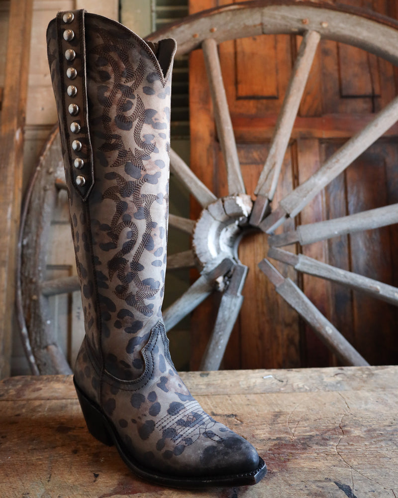 Leopard print boot with studded details on a wooden surface with a rustic wheel background