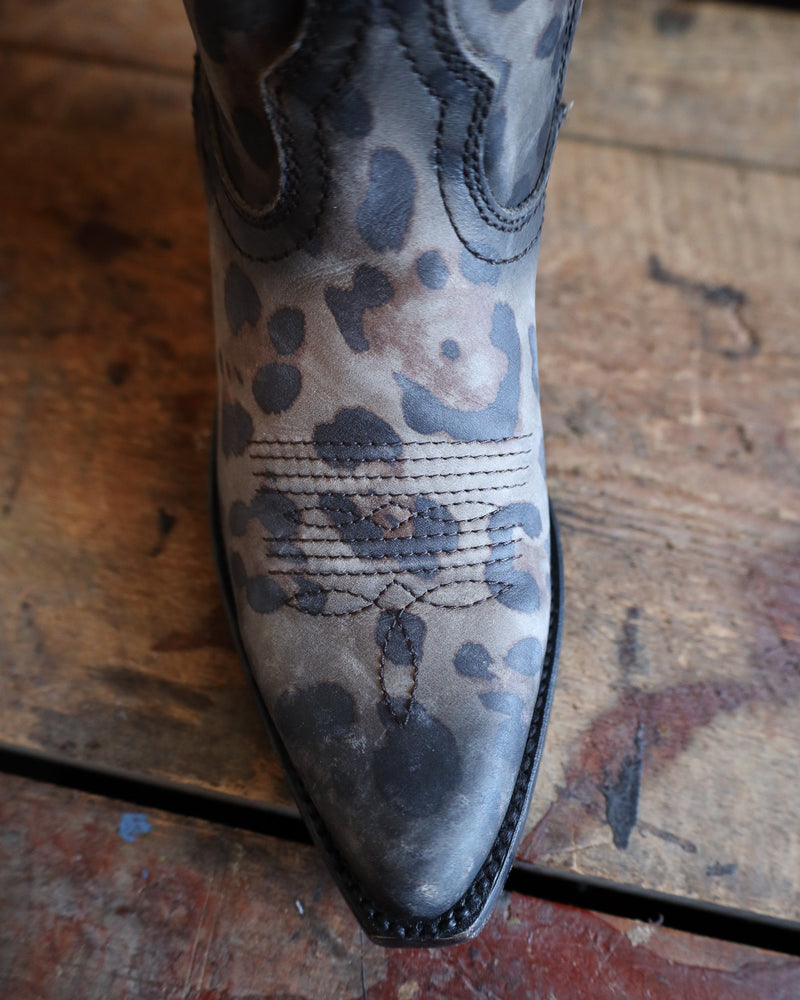 Close-up of a cowboy boot with floral patterns on a wooden floor.