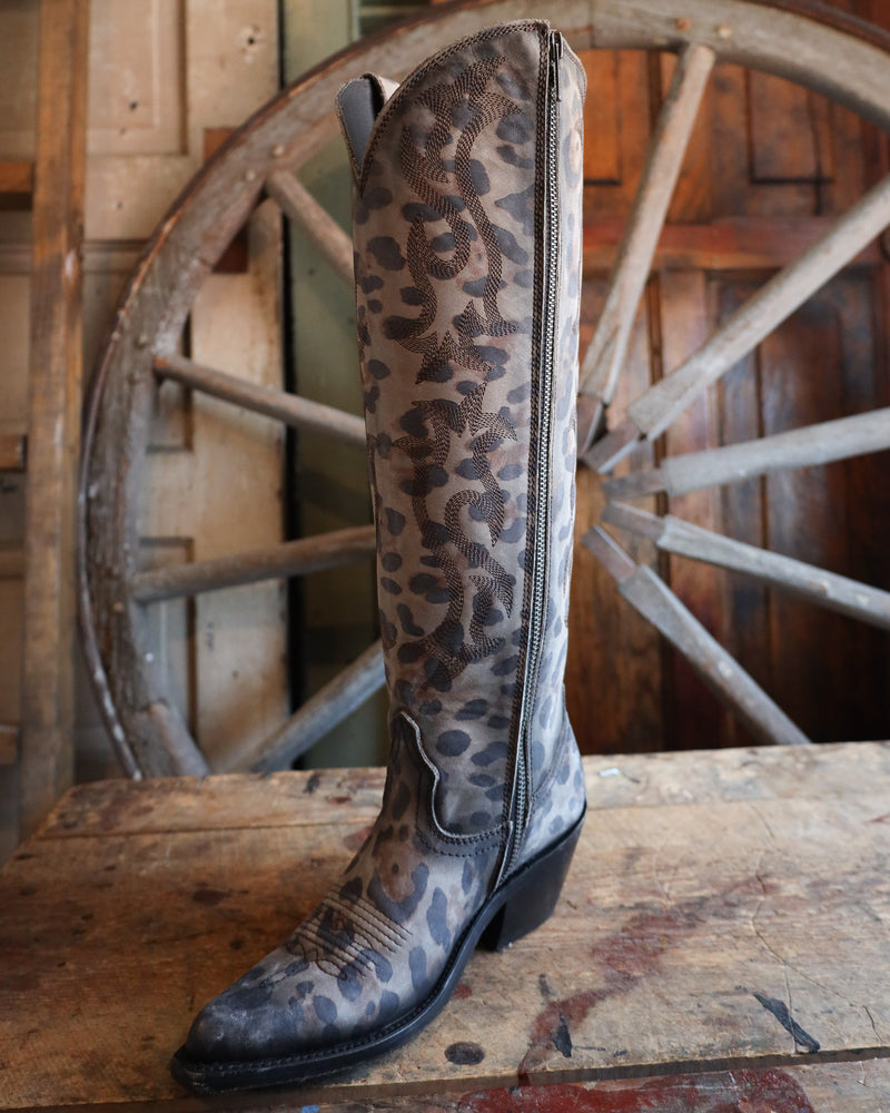Leopard print boot on a wooden surface with a rustic wheel in the background