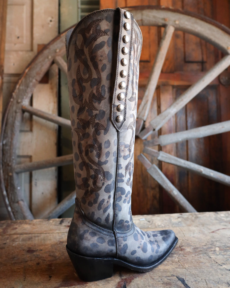 Leopard print cowboy boot with studded detail on a wooden surface with a rustic background.