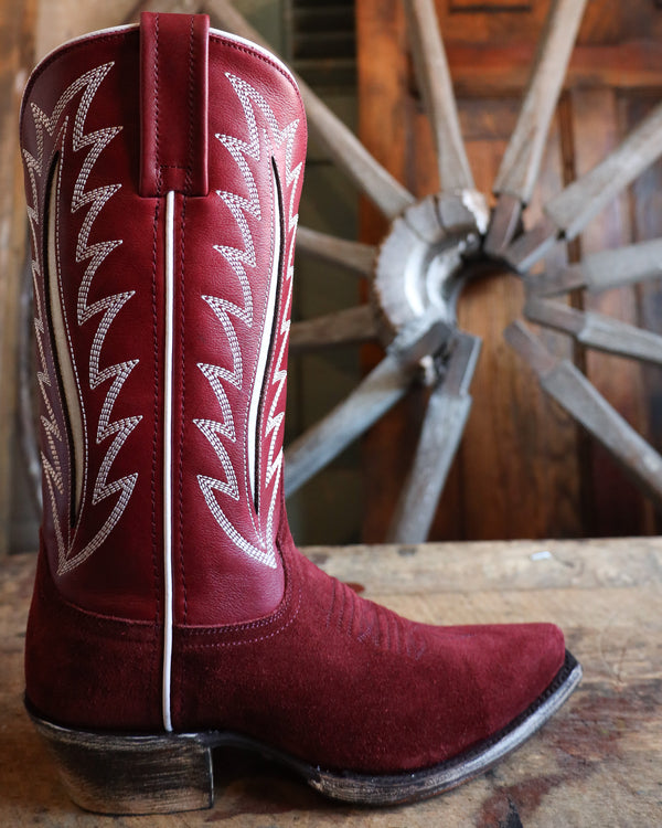 Red cowboy boot with white stitching on a wooden surface with a wheel in the background