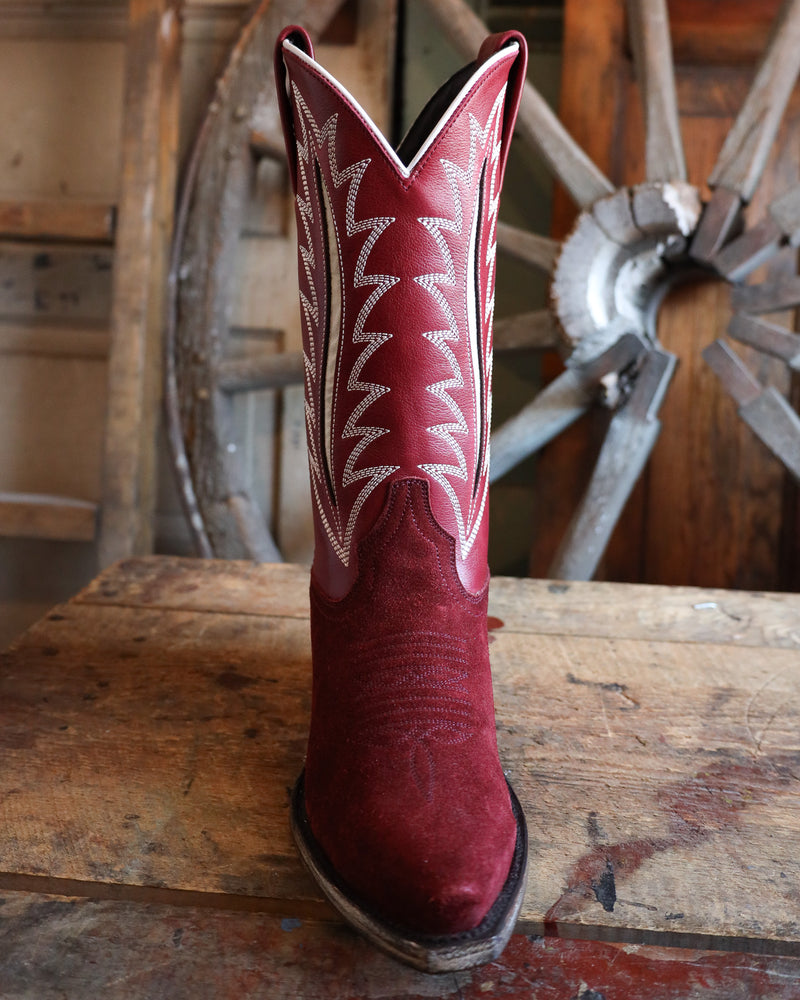 Red cowboy boot with white stitching on a wooden surface with a rustic background