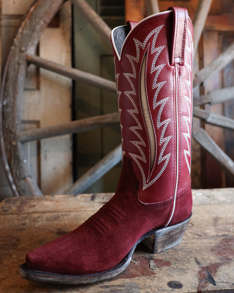 Red cowboy boot with white stitching on a wooden surface with a rustic background