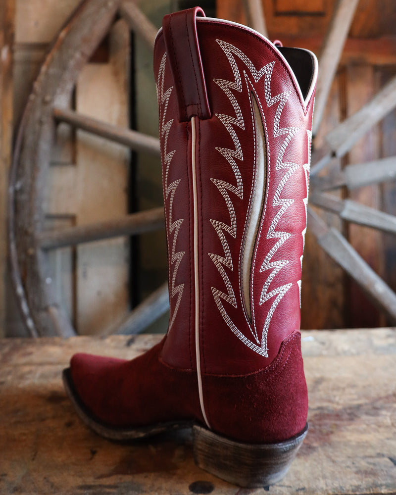 Red cowboy boot with white stitching on a wooden surface