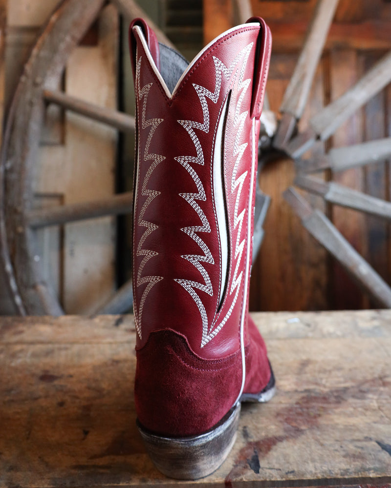 Red cowboy boot with white stitching on a wooden surface