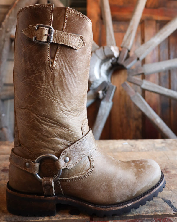 Brown leather boot with a buckle on a wooden surface with a rustic background