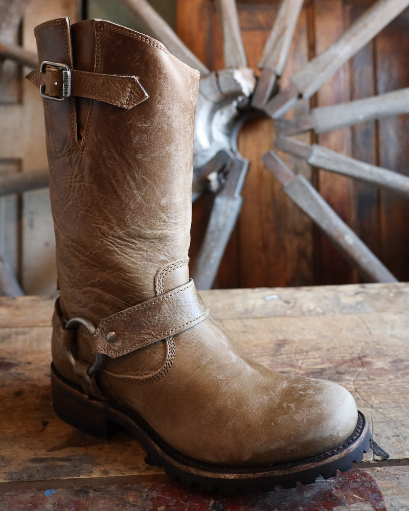 Brown leather boot with a strap on a wooden surface with a wheel in the background