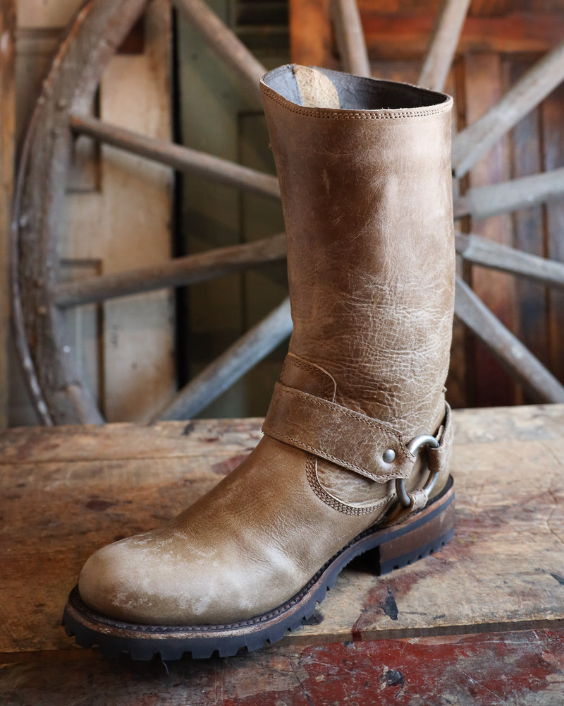 Brown leather boot with a strap on a wooden surface with a rustic background