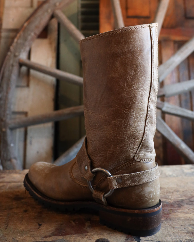 Brown leather boot with a strap on a wooden surface with a rustic background