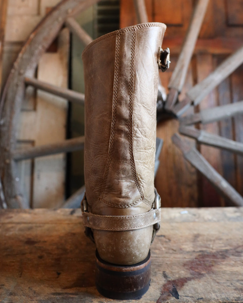 Brown leather boot with a metal buckle on a wooden surface with a rustic background