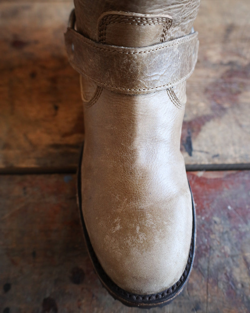 Close-up of a beige boot with a strap on a textured surface