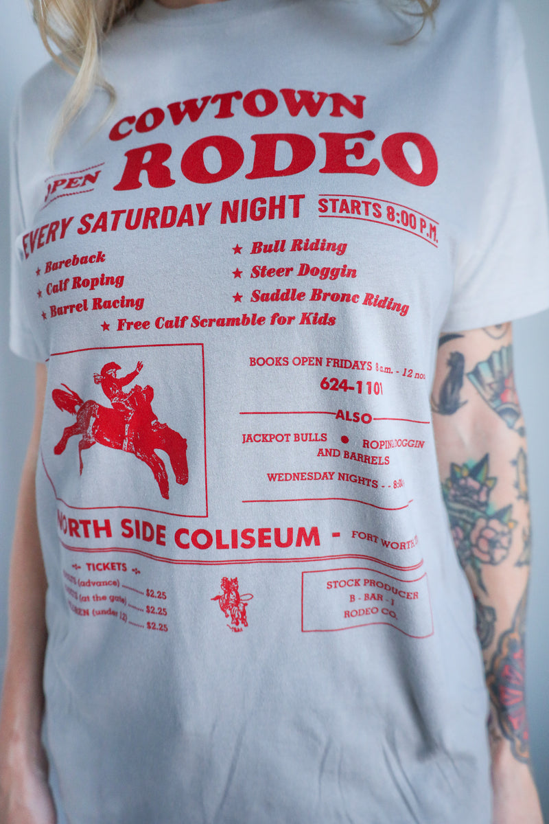 White t-shirt with red 'Cowtown Rodeo' graphic design on a person wearing a tattooed arm.