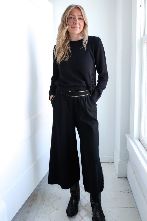 Woman wearing a black outfit with wide-leg pants in a bright room.