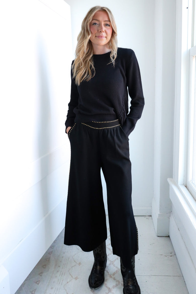 Woman wearing a black outfit with wide-leg pants in a bright room.