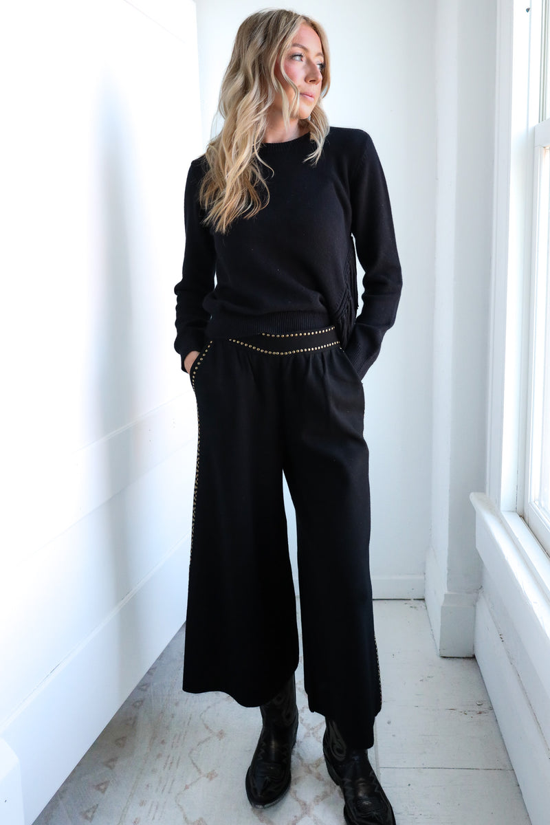 Woman wearing a black outfit with wide-leg pants in a bright room.